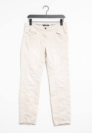 Beige casual broek met voorzakken hangend aan een zwarte plastic hanger tegen een witte achtergrond.