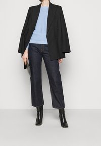 Svart dubbelknäppt blazer över en ljusblå tröja, kombinerat med mörka denimbyxor i cropped-modell och svarta klackstövlar. Enkel kuvertväska i handen.