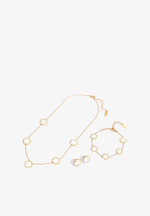 Gold jewelry set with white flower-shaped accents, including a necklace, bracelet, and a pair of stud earrings on a white background.