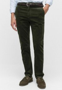 Oliwkowe spodnie kordowe o slim fit, z bocznymi kieszeniami, plecionym brązowym paskiem i brązowymi zamszowymi butami żeglarskimi.