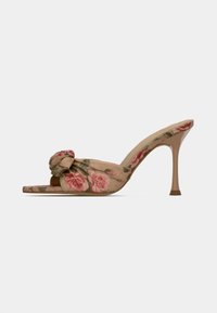 Mules de tacón alto con estampado floral en tela beige, con un detalle de nudo en la parte frontal y un tacón delgado y cónico.