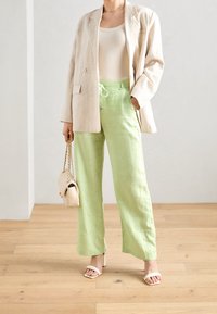 Béžový lněný blejzr, přiléhavý bílý tílko, světlezelené kalhoty s širokými nohavicemi a stahovacími šňůrkami v pase, a světlé sandály na podpatku. Malá kabelka.