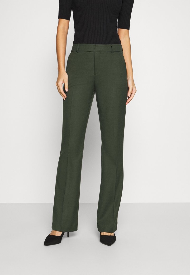 Femme portant un pantalon droit vert foncé et des talons noirs à bout pointu, associé à un top noir côtelé ajusté.