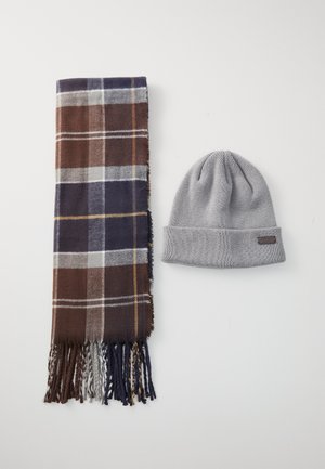 Écharpe à carreaux marron et marine avec des bords frangés à côté d'un bonnet en tricot gris clair avec un revers et une petite étiquette en tissu.
