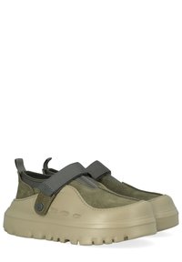 Scarpe in camoscio conciato al vegetale e materiali sintetici di colore verde oliva, con suola beige testurizzata e cinturino regolabile grigio per una calzata sicura.