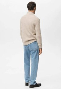 Be�żowy sweter z dzianiny z kołnierzem szalowym, zestawiony z jasnoniebieskimi jeansami i czarnymi butami, pokazujący fakturowaną tkaninę i luźny krój.