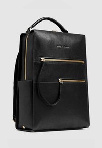 Sac à dos en cuir noir avec fermetures éclair dorées, design structuré, poignée supérieure, poches avant et surface texturée. Deux fermetures éclair latérales pour l'accès.