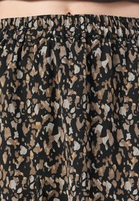 Tissu noir avec un motif abstrait tacheté beige et marron clair et une ceinture froncée, porté à la taille montrant la peau abdominale au-dessus.
