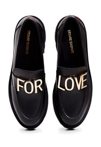 Mocassins en cuir noir ornés de lettres dorées formant "FOR" sur la chaussure gauche et "LOVE" sur la chaussure droite, avec le nom de la marque à l'intérieur.