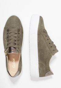 Zielone zamszowe trampki z białą gumową podeszwą, wyposażone w sznurowanie, złoty zamek błyskawiczny oraz metaliczny akcent na pięcie.