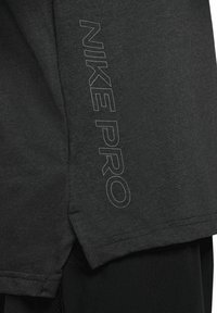 Maglietta atletica nera realizzata in tessuto morbido. Presenta il logo "NIKE PRO" in grigio sul lato. Maniche corte con una vestibilità comoda e dettaglio sull'orlo.