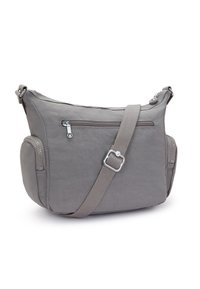 Szara torba crossbody o gładkiej, matowej teksturze. Ma kieszeń z zamkiem z przodu, regulowany pasek oraz zaokrąglony dół z kieszeniami bocznymi.