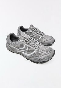 Paire de baskets de sport grises avec tissu en mesh, lacets et motif chevron blanc sur fond blanc.