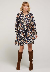 Robe à motif floral en bleu marine avec des accents beiges et rouilles, présentant un devant à boutons, des manches longues et une jupe à niveaux.