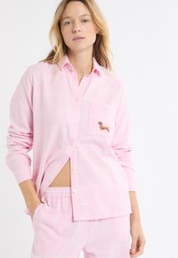 Różowy zestaw piżam w kratę, składający się z koszuli zapinanej na guziki z kieszenią na piersi i haftowanym wzorem psa oraz spodni z elastycznym paskiem.