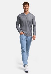 Camisa henley gris de manga larga con un cuello blanco contrastante, combinada con jeans azul claro y zapatillas blancas, mostrando un look casual.