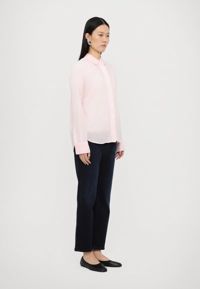 Chemise rose clair à manches longues avec fermeture à boutons, associée à un jean droit bleu marine et des ballerines noires. Tissu doux, coupe ajustée.