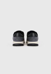 Zwarte en grijze sneakers met een combinatie van leer en suède, voorzien van een comfortabele zool en een logo op de hiel.