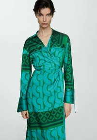 Rochie verde învelită, confecționată dintr-un material neted. Prezintă modele geometrice în nuanțe variate, cu mâneci lungi și decolteu în V.