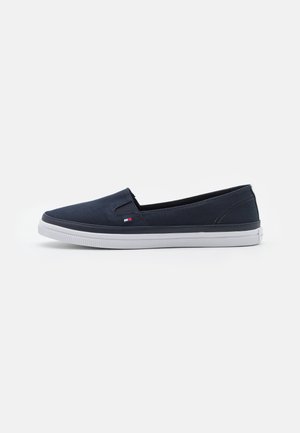 Navy blue slip-on canvas shoe with white rubber sole and small red, white, and blue logo on the side, shown in profile.