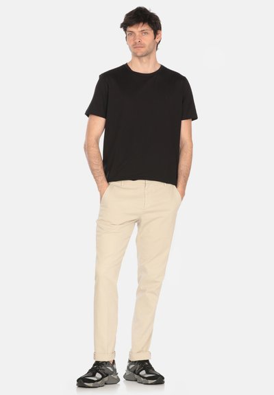 T-shirt nera in cotone abbinata a pantaloni chinos beige. Il modello indossa sneaker sportive nere e grigie, stando in modo disinvolto con le mani in tasca.