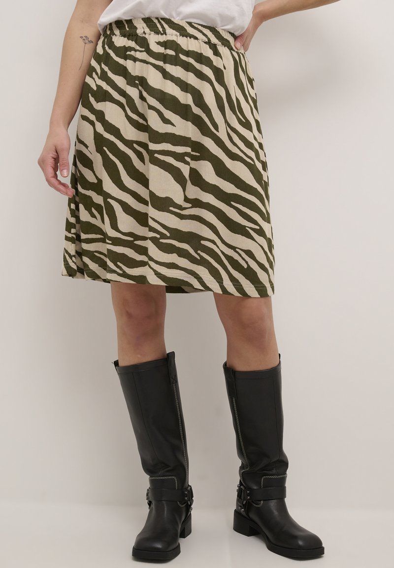 Jupe verte et beige à rayures de zèbre, longueur genou avec taille élastique, associée à des bottes noires montantes avec boucles et fermetures éclair.