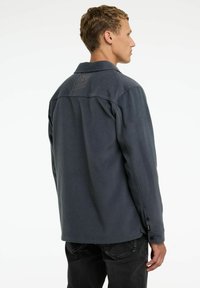 Cămașă button-up de culoare gri închis, cu un material texturat, guler și un detaliu la spate. Are manșete cu nasturi și un design cu croială lejeră.