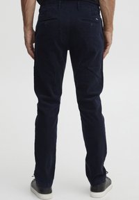 Pantaloni in velluto a coste blu navy con vestibilità slim, tasche posteriori e dettagli cuciti; abbinati a scarpe da ginnastica nere.