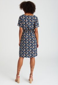 Abito a maniche corte, lunghezza ginocchio, con base blu navy e motivo floreale nei colori rosa, crema e blu. Presenta una vita con cintura e una vestibilità morbida.