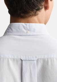 Chemise à rayures bleu clair avec col classique, détail de boutons au dos et un pli subtil pour une texture supplémentaire.