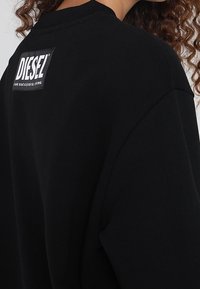 Black sweatshirt featuring a ribbed crew neckline and oversized fit, with a white Diesel logo patch on the back.