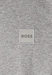 Γκρίζο ύφασμα με υφή που διαθέτει ένα τετράγωνο κομμάτι με τη λέξη "BOSS" σε σκούρο γκρι γράμμα.