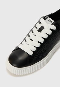 Fekete bőr sneaker fehér gumitalppal és fűzőkkel. Az oldalon dombornyomott logóval és lekerekített orrrésszel rendelkezik.