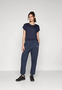 Mörkblå t-shirt med kort ärm och avslappnad passform, kombinerad med mörkblå sweatpants med dragsko i midjan och logotypdetalj, bärs med svarta sneakers.