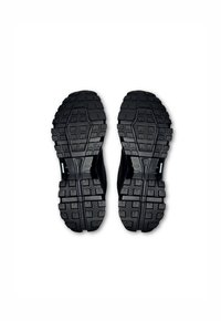 Chaussures de sport noires avec des semelles en caoutchouc texturé et des crampons profonds, conçues pour une meilleure adhérence. La partie supérieure comprend des sections découpées pour la respirabilité.