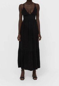 Robe maxi noire avec un corsage ajusté, décolleté en V et fines bretelles. Dotée d'une jupe à volants et d'un tissu doux et fluide. Sandales noires à lanières.