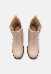 Bottes beige à la cheville en cuir lisse avec un bout arrondi, des panneaux latéraux élastiques, et une languette au talon. Semelle en caoutchouc marron, coutures minimalistes.