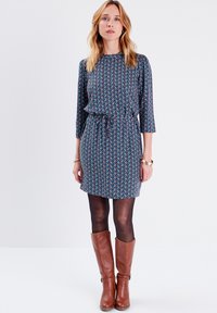 Vestido de patrón floral en azul oscuro, con mangas de tres cuartos y cintura ajustada. Combinado con botas de cuero marrón hasta la rodilla.