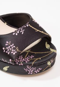 Sandale compensée en satin noir à bout ouvert avec broderie florale rose et dorée et large bride sur le pied.