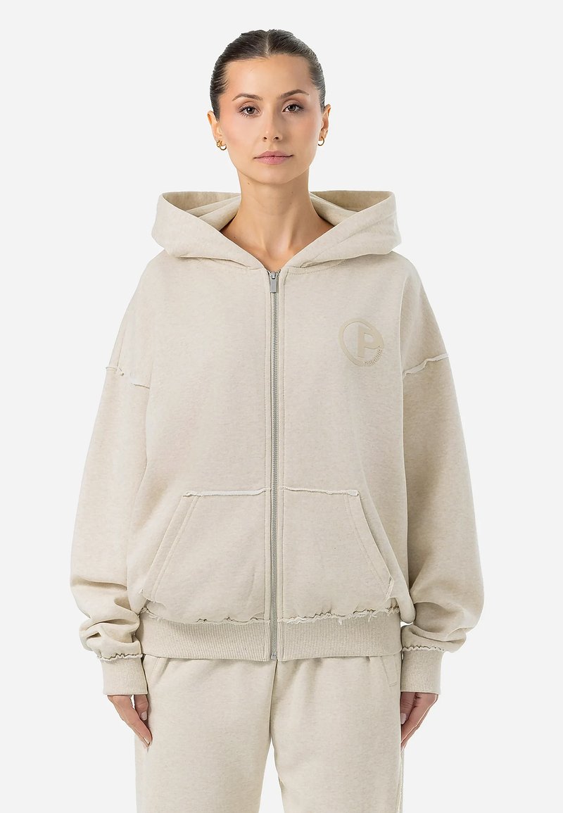 Felpa con zip color beige chiaro realizzata in tessuto morbido e texturizzato. Presenta un cappuccio con coulisse, tasche frontali e un logo discreto sul petto.