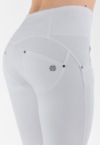 I pantaloni in denim bianco presentano una vita alta, tasche posteriori curve con dettagli in metallo e una finitura testurizzata. Cuciture eleganti lungo le cuciture.