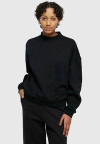 Svart genser med høy hals, oversized passform og ribbede ermer. Stoffet er glat, med en matt finish og uten synlige mønstre.