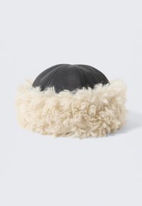 Czarna skórzana czapka z puszystym beżowym futerkiem syntetycznym. O zaokrąglonym kształcie z przeszyciami na czubku. Ogólnie miękka faktura.