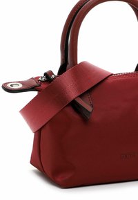 Red handbag made of textured fabric, featuring short handles, a long strap, and a metal snap closure. Embossed logo detail on the side.