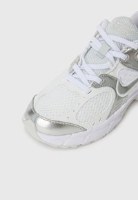 Chaussure de sport blanche avec des accents argentés. Comprend un dessus en mesh, un bout rond, un col rembourré et des lacets plats. Semelle texturée pour une meilleure adhérence.