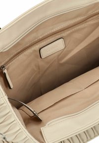 Intérieur d'un sac à main beige avec un tissu lisse, comprenant une poche zippée, une étiquette, et des compartiments spacieux pour l'organisation.
