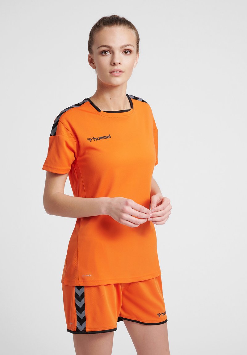 Orange atletisk trøje og shorts sæt med sorte accenter. Trøjen har en rund hals og logo. Shortsene har et chevron mønster på siderne.