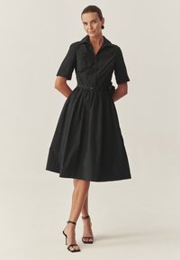 Čierne bavlnené šaty s gombíkovou prednou časťou, krátkymi rukávmi, zúženým pásom a plnou sukňou. Obsahuje kvetinový akcent na opasku.