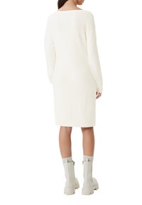 Långärmad klänning i knälängd i off-white stickad tyg, med rundad rygg och ribbade muddarna, i kombination med ljusgrå ankelskor.