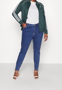 Grön zip-up jacka med vita ränder, tillsammans med blå högmidjade jeans och vita pumps. En enkel vit t-shirt under.